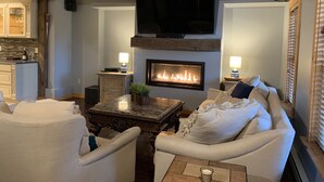 A cozy living room with a fireplace, a television mounted above it, and a comfortable seating area with a sofa and armchairs.