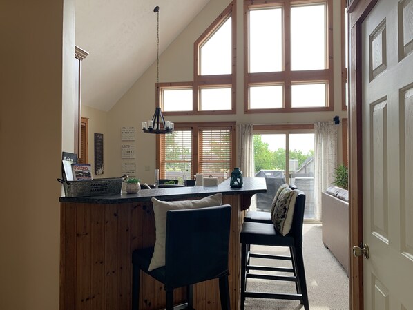 A kitchen with a wooden island, two bar stools, a hanging light fixture, and large windows with blinds. - Beautiful mountain house with incredible views of the Pocono mountains. (Tannersville)