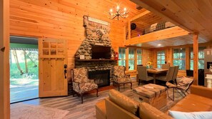 A cozy log cabin interior with a stone fireplace, wooden walls, and a dining area.