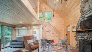 A cozy cabin interior with a wooden staircase, a fireplace, and a seating area with a couch and chairs.