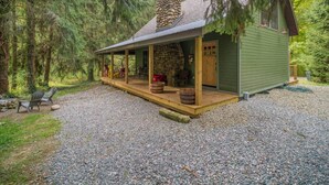 A rustic cabin with a stone chimney, wooden deck, and a covered porch.