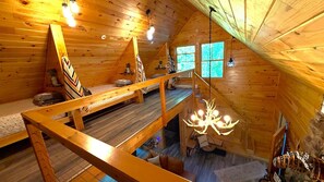 A cabin with a loft bedroom, a staircase, and a chandelier.