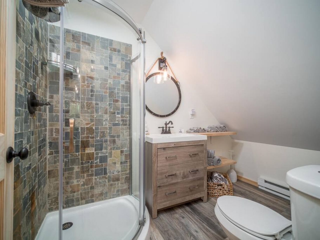 A bathroom with a glass-enclosed shower, a wooden vanity, and a white toilet.