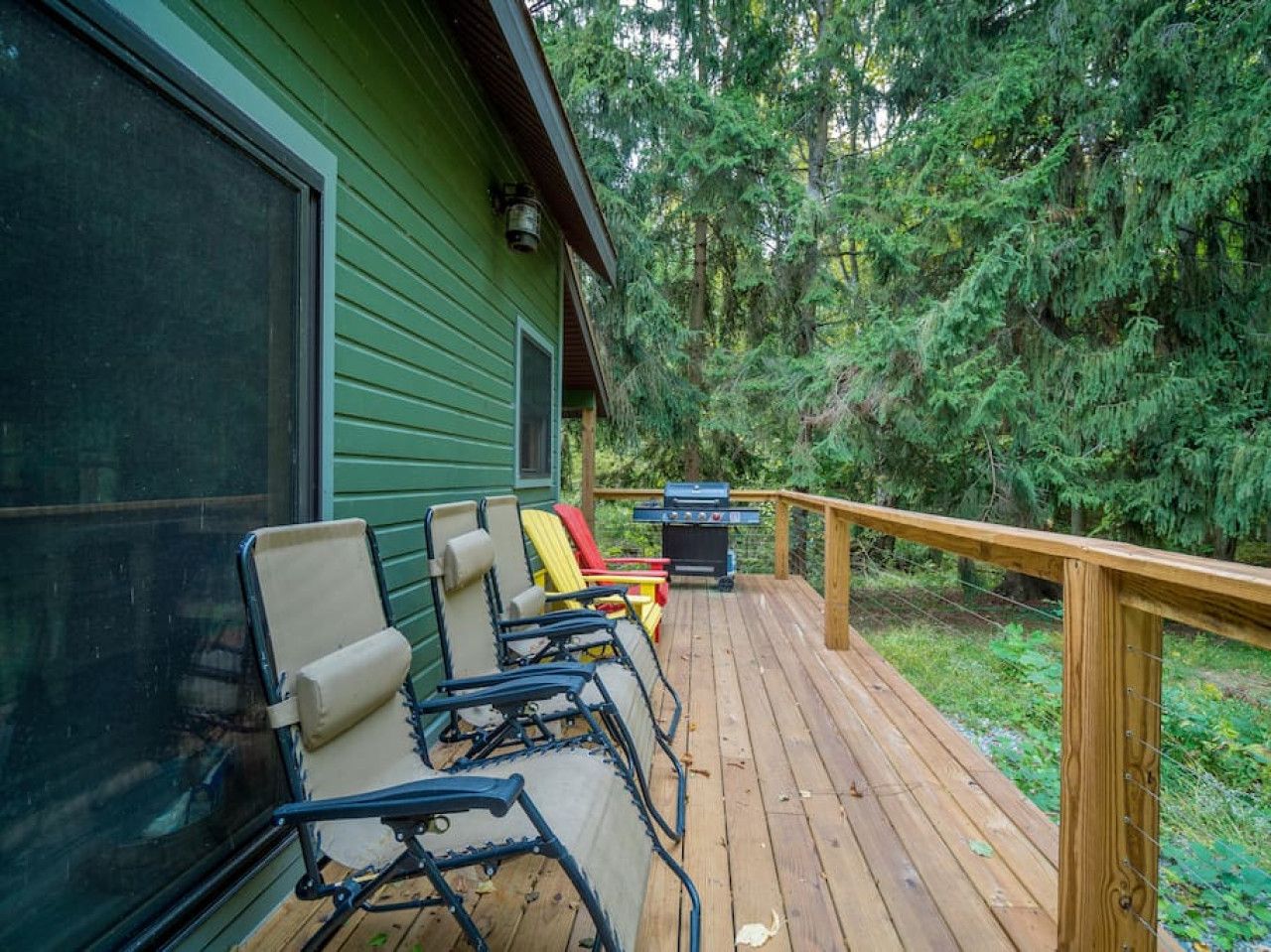 Eine Holzterrasse mit Sitzgelegenheiten und einem Grill, umgeben von dichtem Wald.