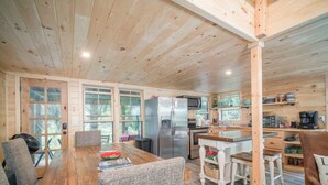 A wooden cabin interior with a dining area, kitchen, and seating.