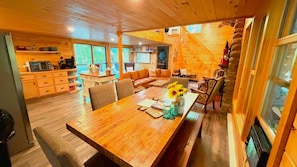 A wooden interior with a dining table, chairs, a sofa, and a kitchen area.