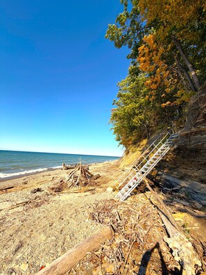 A beach with a pile of driftwood, a ladder, and a rocky cliff.