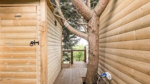 A wooden cabin with a door, a tree in the center, and a wooden deck. - The hideaway  (Bristol)