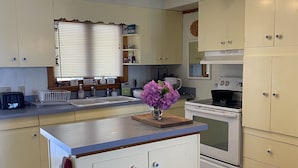 A kitchen with white cabinets, a central island, a stove, and a window with blinds. - Bemus Point Lake Front Cottage with Dock (Bemus Point)