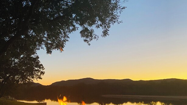 Ein Lagerfeuer mit Flammen, ein Stuhl und ein See mit Bergen im Hintergrund.