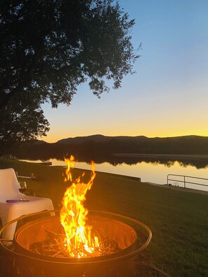 Un braciere con fiamme, una sedia e un lago sullo sfondo con montagne.