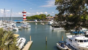 Un puerto deportivo con barcos amarrados, un faro y un árbol en primer plano.