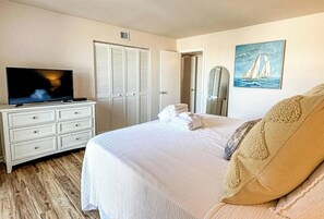 Una camera da letto con un letto, una televisione su un comò, una porta e un quadro appeso al muro.