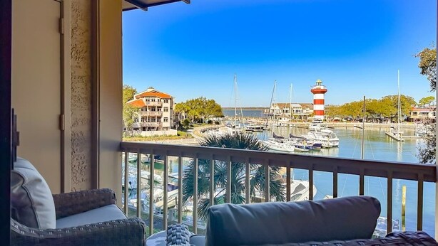 Un balcón con vistas a un puerto deportivo, que incluye barcos y un faro.