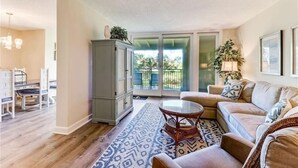 Un salon avec un canapé, une table basse en verre et un tapis à motifs. On y trouve également un meuble et une plante.