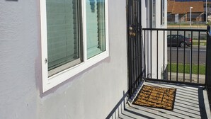 Een woongebouw met een overdekte veranda, een raam met zonwering, een metalen hek en een deurmat.