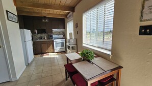 Een keuken met een houten plafond, een eettafel met rode kussens en een raam met zonwering.