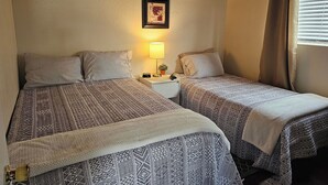 Een kamer met twee bedden, elk voorzien van beddengoed met een patroon, een nachtkastje met een lamp, en lijstjes met afbeeldingen aan de muur.