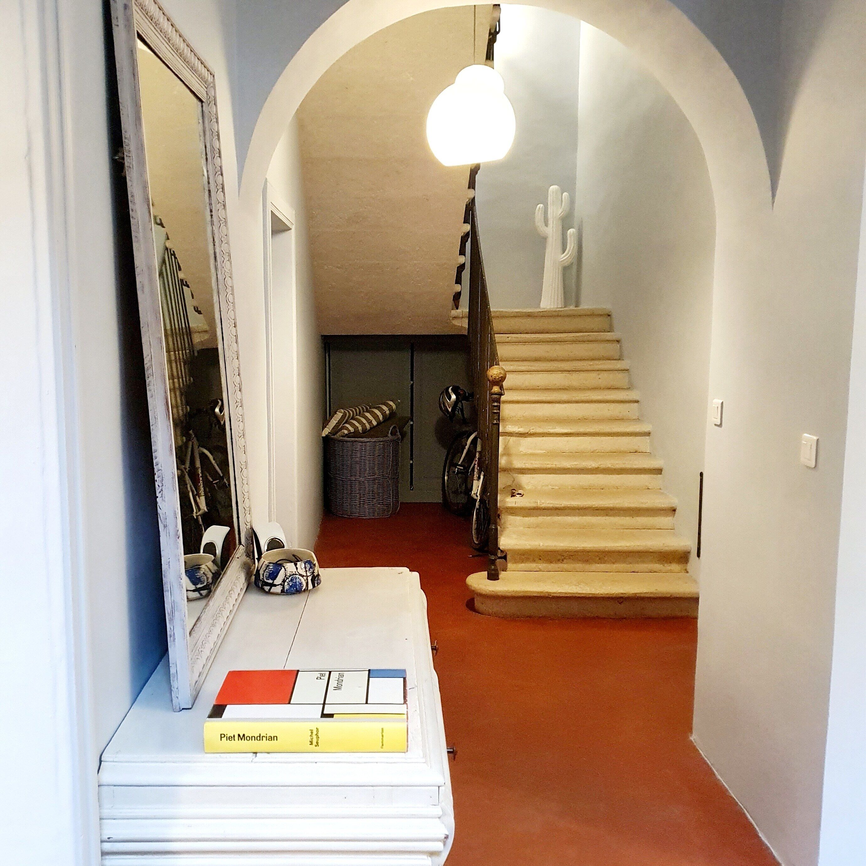 Un couloir avec un escalier, un miroir et quelques objets posés sur une table.