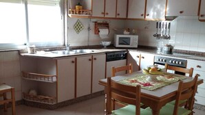 A kitchen with a dining area, featuring a stove, microwave, sink, and wooden cabinets. - Piso Sencillo, Amplio y Todas las Comodidades (O Vicedo)