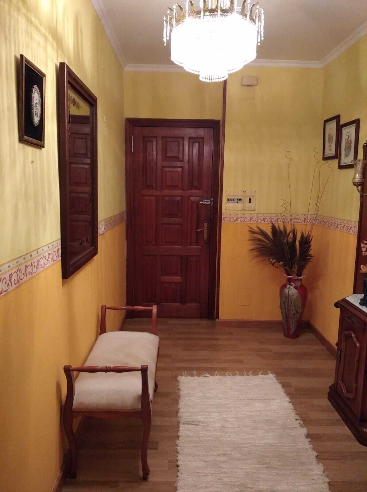 Un corridoio con una porta in legno, una panchina, un lampadario e una pianta in vaso.