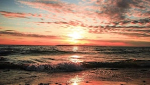 Een strand bij zonsondergang, met golven en een heldere lucht.