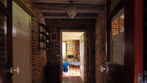 A narrow hallway with brick walls and a tiled floor, leading to a room with a bed and a window. - La Ferme du Pré Martin guest room (La Genevraie)