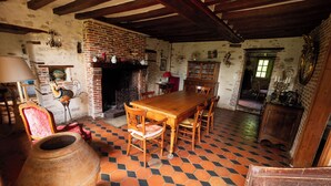 A rustic room with a brick fireplace, wooden dining table, and hexagonal patterned floor. - La Ferme du Pré Martin guest room (La Genevraie)