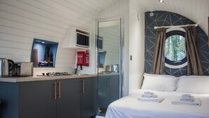 Habitació compacte amb llit, petita cuina i finestra amb cortines.