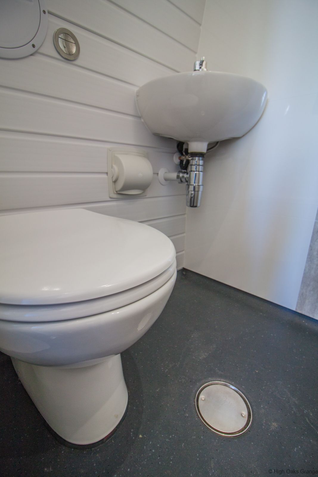 Eine weiße Toilette mit Bidet-Funktion, ein Waschbecken und ein Toilettenpapierhalter auf grauem Boden.