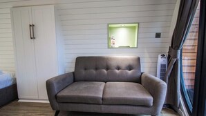 A modern living room with a grey sofa, a white wardrobe, and a wall-mounted light fixture. - Foxtail Glamping Pod - sleeps 2 | Gold Award winning (Pickering)