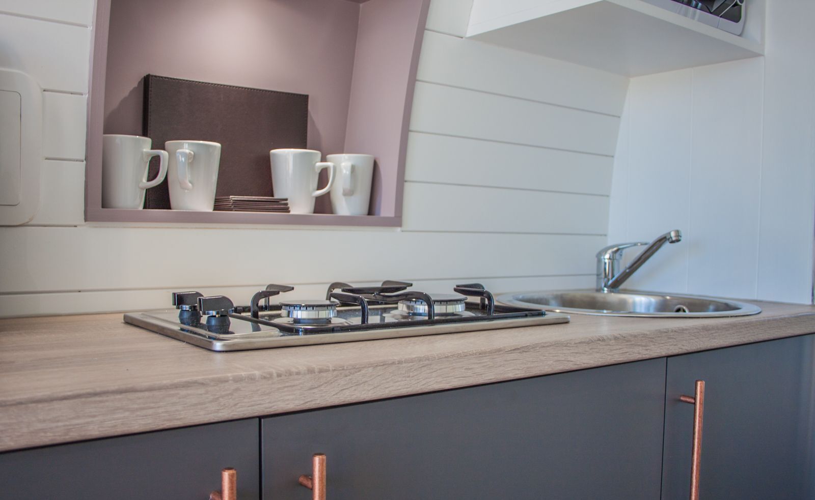 A modern kitchen with a gas stove, a sink, and a shelf with white mugs.