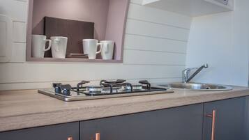 A modern kitchen with a gas stove, a sink, and a shelf with white mugs.