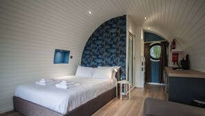 A bedroom with a large bed, a small table, and a view of the kitchen.