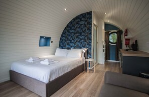 Un dormitorio con una cama grande, una mesita pequeña y vista a la cocina.