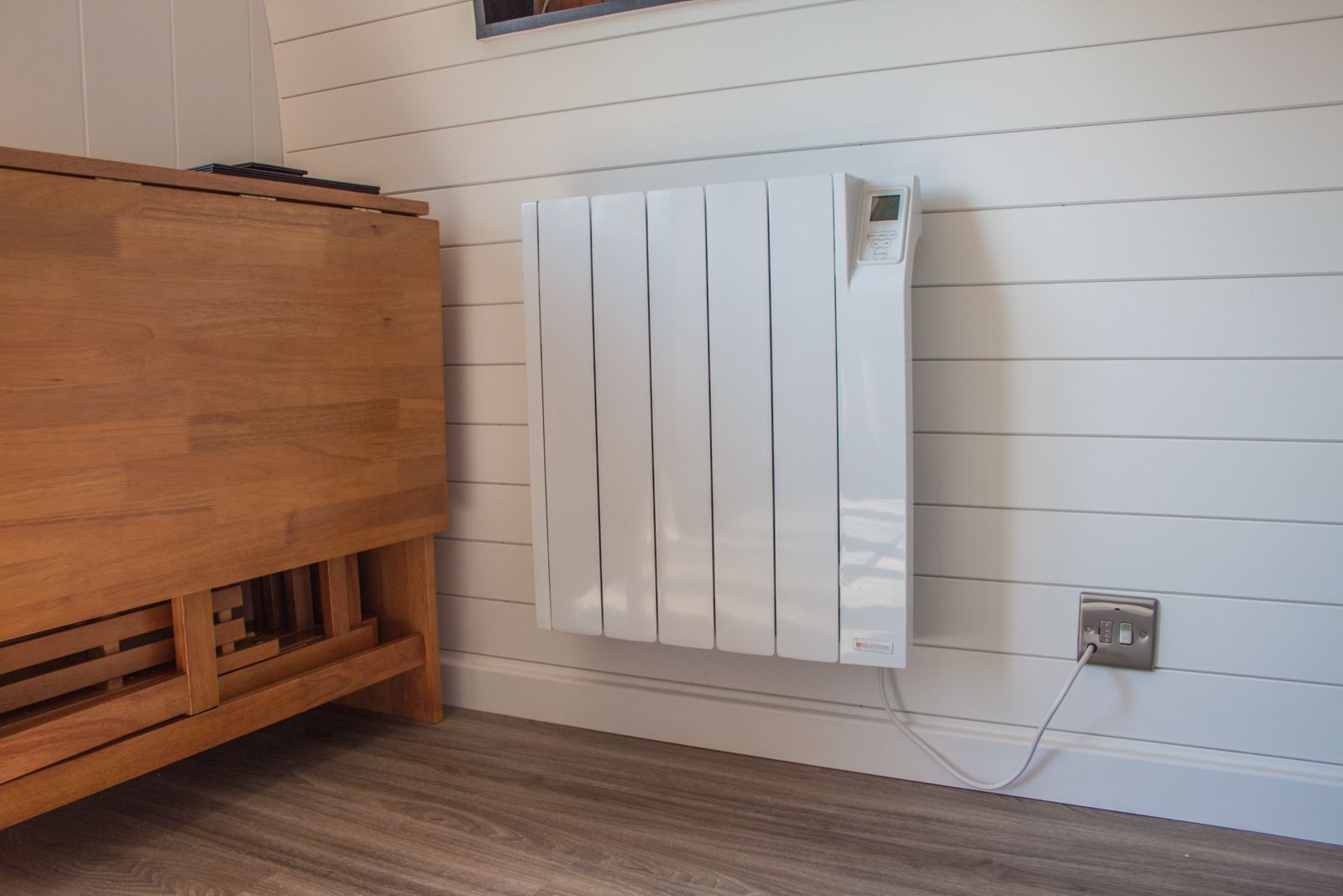 Een witte radiator aan een muur, met een houten kastje eronder.