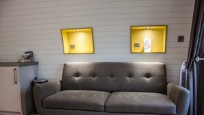 Un canapé gris dans une pièce moderne, avec un mur blanc et un petit meuble placé à gauche.