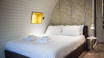 A neatly made bed with folded towels, a bedside lamp, and a wall with a tree pattern.