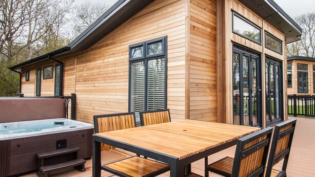 Una cabaña de madera con jacuzzi, terraza y zona de comedor con sillas y mesa.