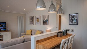 Una sala de estar moderna con una mesa de comedor de madera, sillas blancas, un sofá con cojines amarillos y un televisor sobre un mueble.
