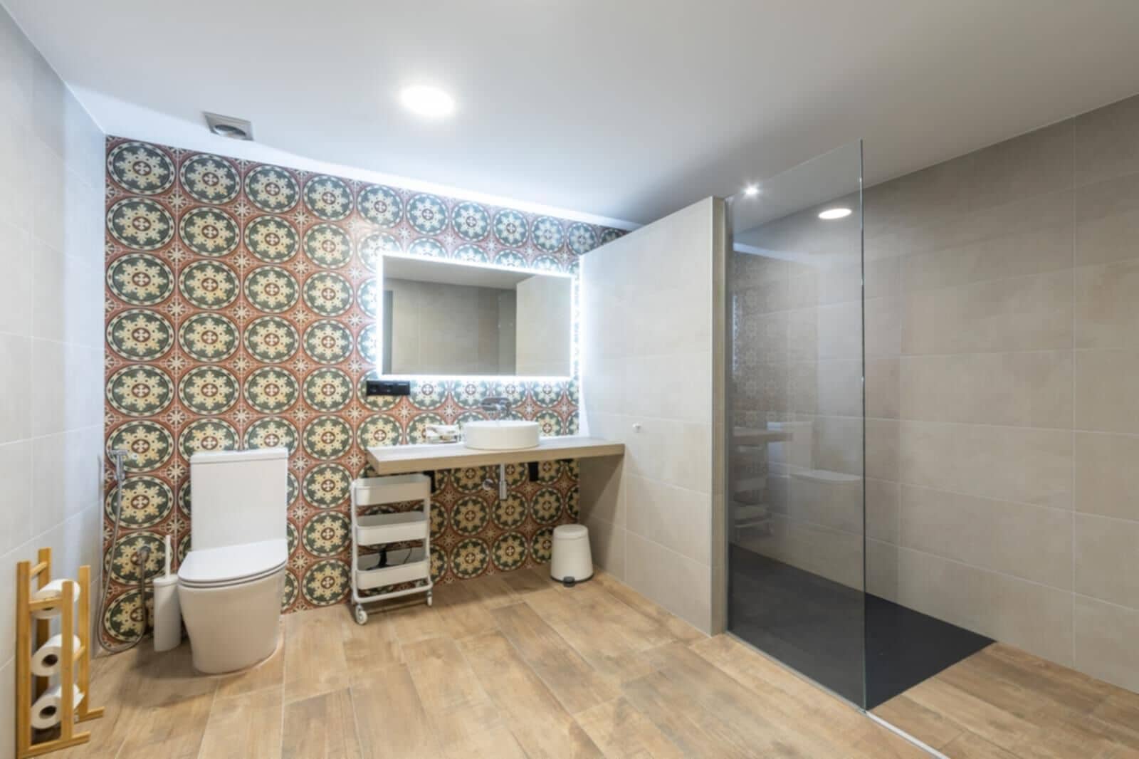 Une salle de bain avec un mur recouvert de carreaux décoratifs, des toilettes, un lavabo avec un miroir et une douche en verre.