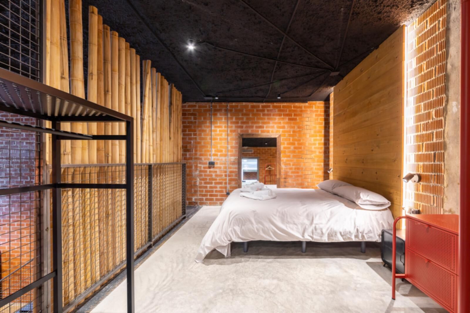 Un dormitorio con pared de ladrillo, cama con ropa blanca y un radiador rojo.