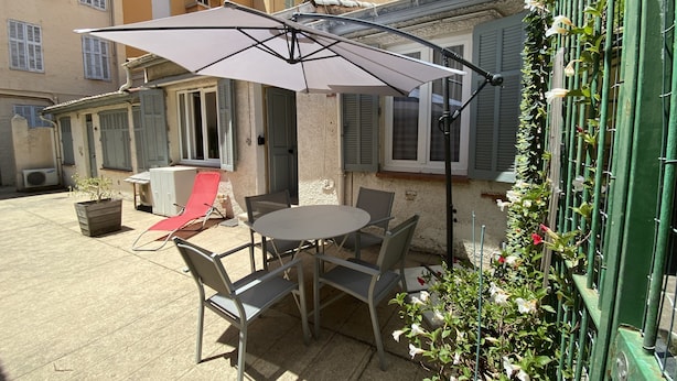 Un patio al aire libre con una mesa, sillas, un paraguas grande y una planta en maceta.