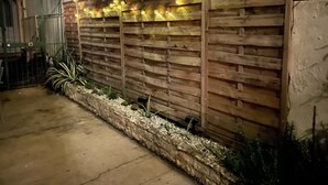 Una pared de madera con luces de cuerda, una jardinera de piedra y una reja metálica.