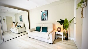 Una sala de estar moderna con un sofá blanco, cojines color turquesa, una mesita de noche con una lámpara y una planta grande en maceta.