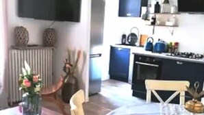 Een eetgedeelte met een tafel en stoelen, een tv aan de muur en een keuken op de achtergrond.