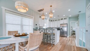 A modern kitchen with white cabinets, a stainless steel refrigerator, and a dining area with wicker chairs and a round table. - Fully Renovated! Gulf AND Bay views! Inground Heated Pool! 2 min walk to beach! (Port St. Joe)
