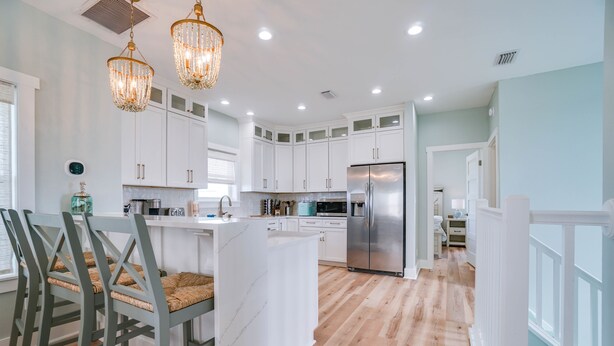 A modern kitchen with white cabinets, a stainless steel refrigerator, and a central island. - Fully Renovated! Gulf AND Bay views! Inground Heated Pool! 2 min walk to beach! (Port St. Joe)