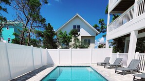 A swimming pool with a tiled deck, surrounded by a white fence, and a two-story building with balconies in the background. - Fully Renovated! Gulf AND Bay views! Inground Heated Pool! 2 min walk to beach! (Port St. Joe)