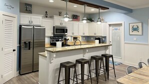 Une cuisine moderne avec des meubles blancs, des appareils en acier inoxydable, un comptoir en granit et un coin bar avec des tabourets.